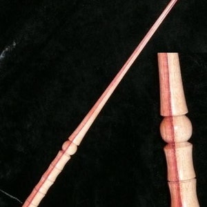 以下が含まれることがあります： ピンクと白の木目模様のついた木製の杖。杖の長さは約76cmで、先端は丸みを帯びています。杖は2つの木片を接合して作られています。