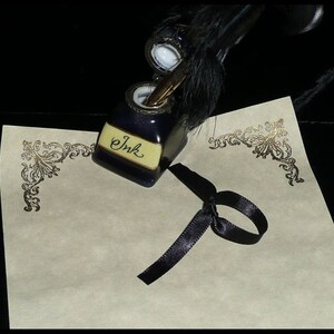May include: A blue inkwell with a quill pen and a black ribbon on a piece of paper with gold filigree. The inkwell has the word "Ink" written on it.