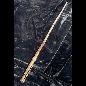 May include: A wooden wand with a dark brown and light brown wood grain pattern. The wand has a decorative, carved handle.
