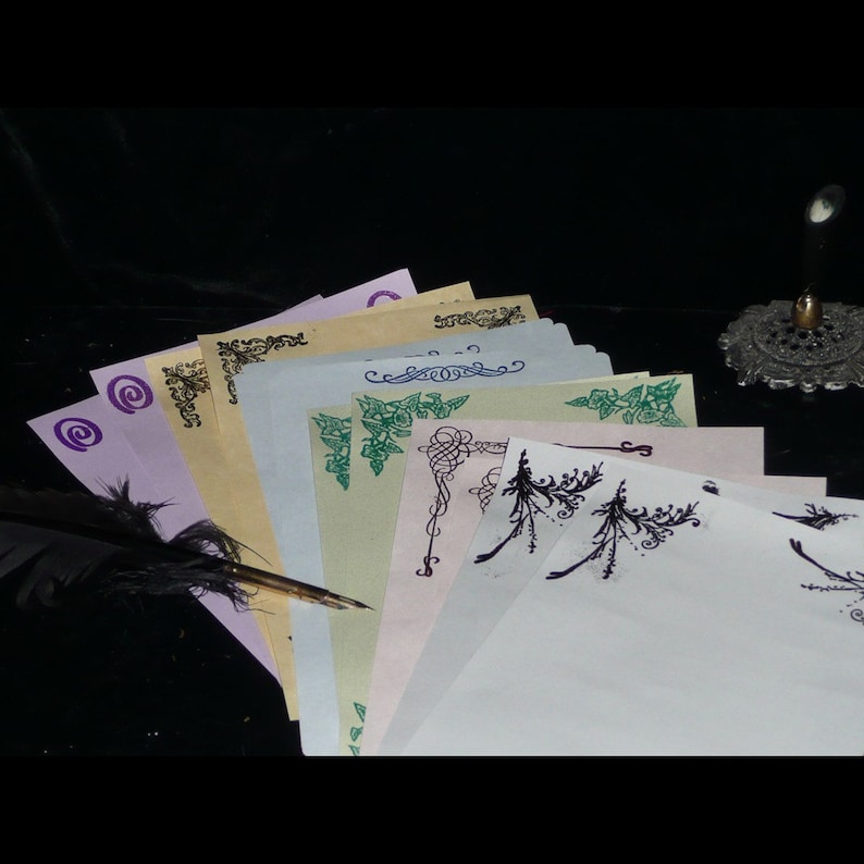 May include: A stack of blank stationery paper with decorative borders in various colors, including green, purple, and black. A quill pen is placed on top of the stack.