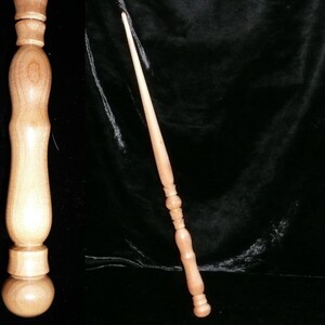 May include: A wooden wand with a light brown finish. The wand has a rounded tip and a thicker base with intricate carvings. The wand is approximately 14 inches long.