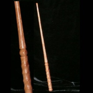 Puede incluir: Una varita de madera de color marrón claro y rosa. La varita tiene una punta redondeada y una serie de pequeños pomos redondos a lo largo del eje.