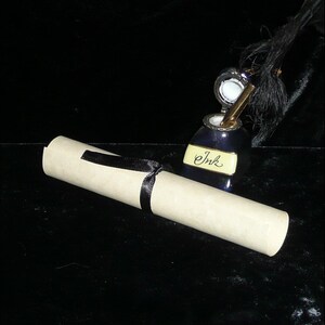 May include: A rolled up piece of parchment paper tied with a black ribbon, next to a blue inkwell with a quill pen and the word "Ink" written on it.