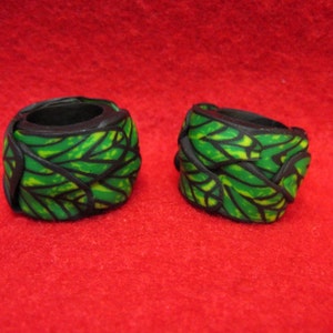 May include: Two black and green patterned rings. The rings are made of polymer clay and have a leafy design.