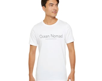 Op de afbeelding: Wit T-shirt met de tekst "Ocean Nomad" en een golvende lijn eronder.