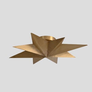 Könnte beinhalten: Eine goldfarbene Deckenleuchte in Sternform. Die Leuchte hat mehrere dreieckige Spitzen, die von einer zentralen kreisförmigen Basis ausgehen. Das Metall hat eine gebürstete Oberfläche, und das Gesamtdesign ist geometrisch und modern.