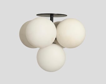May include: A ceiling light fixture featuring four spherical white glass globes arranged in a cluster. The globes are attached to a central black metal stem and a circular black mounting plate, creating a balanced and symmetrical lighting design.