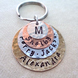 May include: A gold, silver, and copper layered keychain with the names "Alexandra", "Terry", "Jackson", "Shelby", and the initial "M" engraved on the discs.