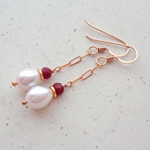 May include: A pair of gold earrings with a white pearl and a red gemstone on each earring.