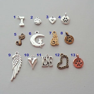May include: Thirteen silver and bronze charms with various designs, including a bone, paw print, heart, cat, crescent moon, cat, angel wings, heart, the word "LOVE", heart, and paw print.