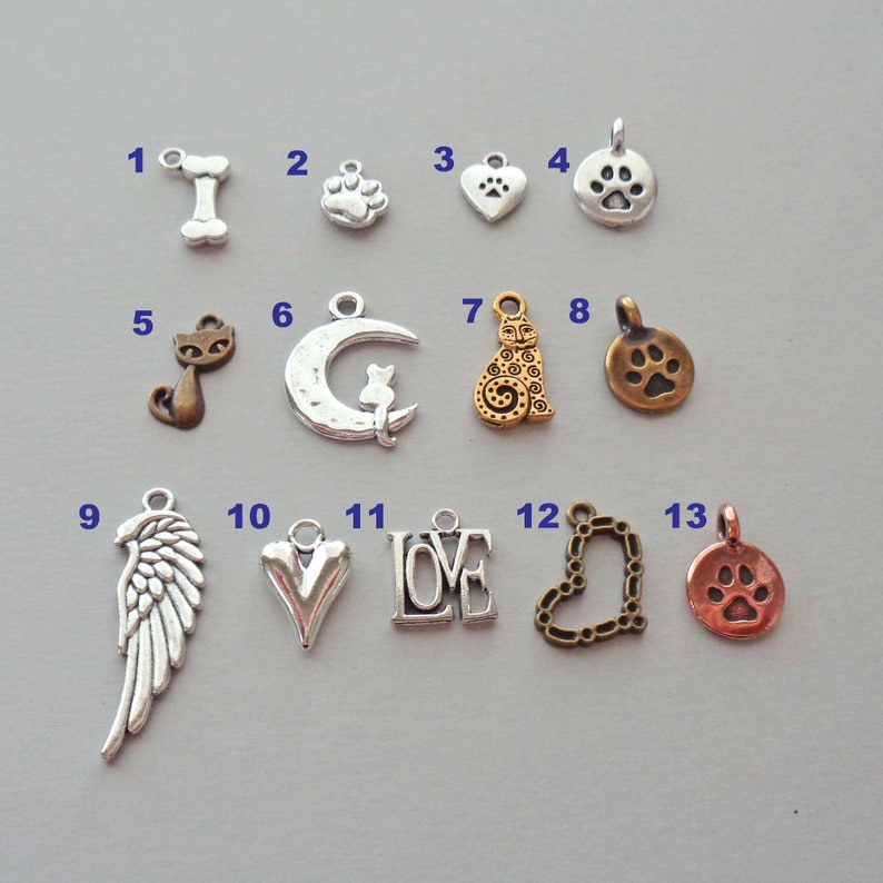 May include: Thirteen silver and bronze charms with various designs, including a bone, paw print, heart, cat, crescent moon, cat, angel wings, heart, the word "LOVE", heart, and paw print.