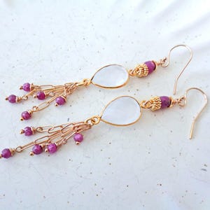 May include: Gold dangle earrings with a teardrop shaped clear stone and a fringe of pink beads and gold chains.