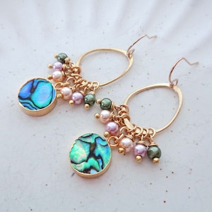 May include: Gold hoop earrings with a round abalone shell charm and a dangling chain of pink and green beads.