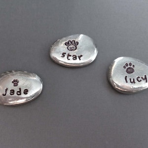 May include: Three silver-coloured metal tokens with paw prints and names engraved on them. The names are "Jade", "Star", and "Lucy".