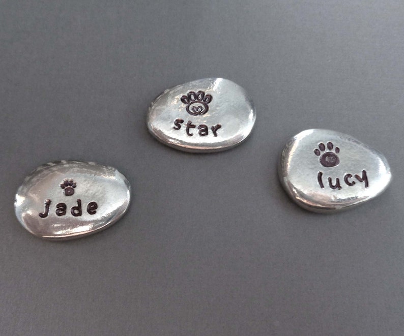 May include: Three silver-coloured metal tokens with paw prints and names engraved on them. The names are "Jade", "Star", and "Lucy".
