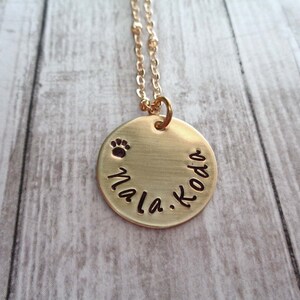 May include: Gold necklace with a round pendant that says "Nala. Koda" with a paw print above the names.