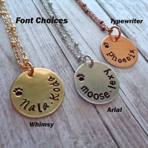 May include: Three gold, silver and copper necklaces with round pendants. Each pendant has a different font style and says "Nala.Koda", "Moose.let", and "phoenix". The necklaces are on a wooden surface with the words "Font Choices", "Whimsy", "Typewriter", "Arial" written below each necklace.