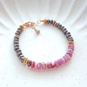 May include: A bracelet made with gray and gold beads and pink gemstone beads.