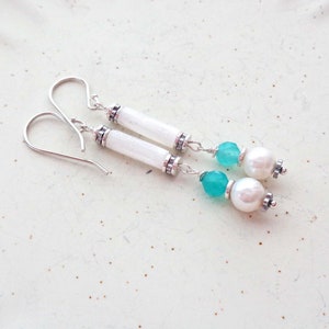 May include: A pair of dangle earrings with white and turquoise beads. The earrings feature a white cylindrical bead with silver accents, followed by a turquoise bead and a white pearl bead.