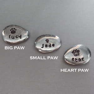 May include: Three silver metal pet memorial stones with paw prints and names. The stones are labelled "Big Paw", "Small Paw", and "Heart Paw".