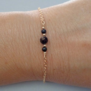 May include: A delicate gold chain bracelet with three black gemstone beads. The center bead is larger and faceted.