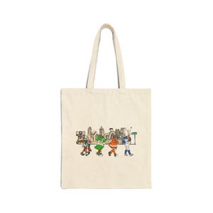 May include: A cream-colored tote bag featuring a colorful illustration of a city skyline and several cartoon figures walking across a street. The figures are dressed in various outfits, and the bag has long handles.