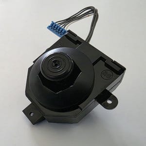 May include: A black joystick component with a circular top and a hexagonal base. It has a blue connector with multiple pins and several black wires extending from the top. The component is set against a white background.