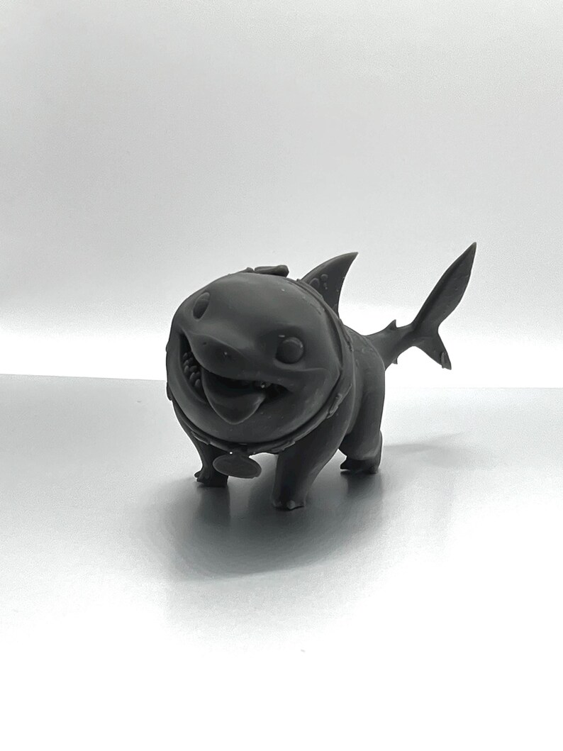 Peut inclure: Une figurine d'un requin en 3D imprim&eacute;e en noir avec un collier de chien et une &eacute;tiquette. Le requin a une expression amicale et est debout sur ses quatre pattes.