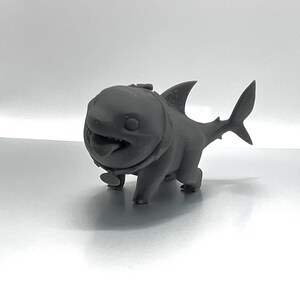 Peut inclure: Une figurine de requin en 3D imprim&eacute;e en gris, avec un collier, marchant &agrave; quatre pattes.