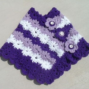 Pode incluir: Poncho de crochê roxo, branco e lavanda com três flores como enfeites.