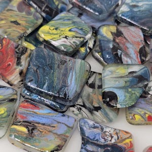 May include: A collection of colorful, square glass tiles with swirled patterns. The tiles feature a mix of colors, including blue, yellow, red, and black, creating a marbled effect. The glass has a glossy finish.