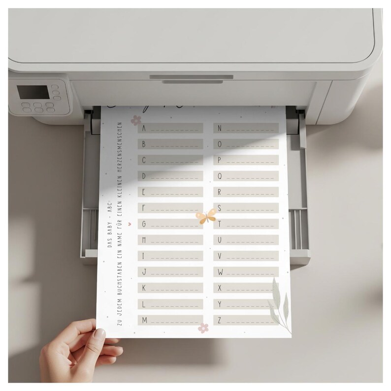 May include: A sheet with German text, including "DAS BABY - ABC ZU JEDEM BUCHSTABEN EIN NAME F&Uuml;R EINEN KLEINEN HERZENSMENSCHEN", is being printed from a white printer. The sheet has a beige background with floral and butterfly accents and lettered boxes.