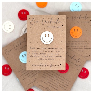 Könnte beinhalten: Braune Karten mit einem weißen Smiley und dem Text "Ein Lächeln für unterwegs". Bunte Smiley-Ausschnitte in Rot, Orange und Blau sind verstreut. Die Karten haben handschriftlichen Text.