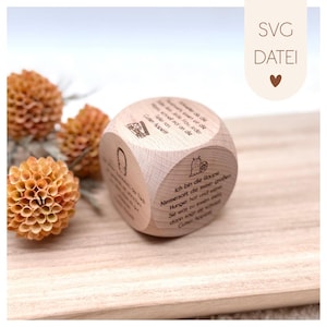 Puede incluir: Un dado de madera con texto e ilustraciones grabadas. El dado presenta varias frases e imágenes, incluyendo una oruga y las palabras "SVG DATEI". El dado se muestra sobre una superficie de madera con flores naranjas secas.