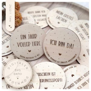 Peut inclure: Ensemble de disques en bois avec texte gravé et motifs de cœur. Les disques présentent des phrases comme "Ein Jahr voller Liebe" et "Ich bin da!" dans une finition bois clair. Certains disques ont du texte en anglais.