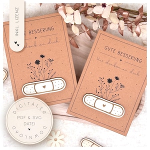 May include: Two brown get-well cards with the phrases "Gute Besserung" and "E Besserung" in script. Each card features a white bandage with a gold outline and a small heart, and a floral design. The cards are decorated with small black hearts.