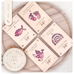 Pode incluir: Cartões de batismo em madeira com vários desenhos, incluindo pegadas, um peixe, um arco-íris e uma pomba, cada um incorporando arte monetária. Os cartões apresentam texto em alemão e estão dispostos em uma bandeja de madeira. Uma etiqueta de download digital redonda também está presente.