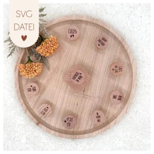 Può includere: Un vassoio di legno con un design circolare, con piccoli gettoni di legno con testo inciso. I gettoni hanno frasi come "Cheers" e "Wine Time". Il vassoio è decorato con fiori secchi e il testo "SVG DATEI".