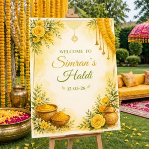 May include: A decorative sign on an easel with the text "Welcome to Simran's Haldi" in gold and green script. The sign is decorated with yellow roses and floral accents. The date 12-03-26 is also displayed. The background includes yellow floral garlands.