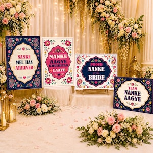 May include: Four decorative signs with floral and paisley designs. The signs have text that reads "NANKE MEL HAS ARRIVED", "NANKE AAGYE KHUSHIYAN LAAYE", "PROUD NANKE OF THE BRIDE", and "TEAM NANKE AAGYE".