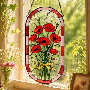 May include: An oval stained glass suncatcher featuring a bouquet of vibrant red poppies with green stems and leaves, tied with a yellow ribbon. The piece is framed by a border of alternating red and light pink glass segments and hangs by a metal chain.