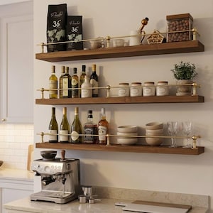 May include: Three-tiered wooden shelves with brass accents, holding coffee, spices, and liquor bottles. A silver espresso machine sits on the counter below. The shelves are mounted on a white wall, creating a stylish kitchen storage solution.