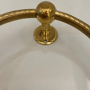 The ring is mounted on a circular base with a ball finial, The design is simple and elegant,The metal has a polished finish, giving it a shiny appearance, The ring is sturdy and well-made, suggesting durability and quality craftsmanship, This decorative piece would add a touch of classic style to any space