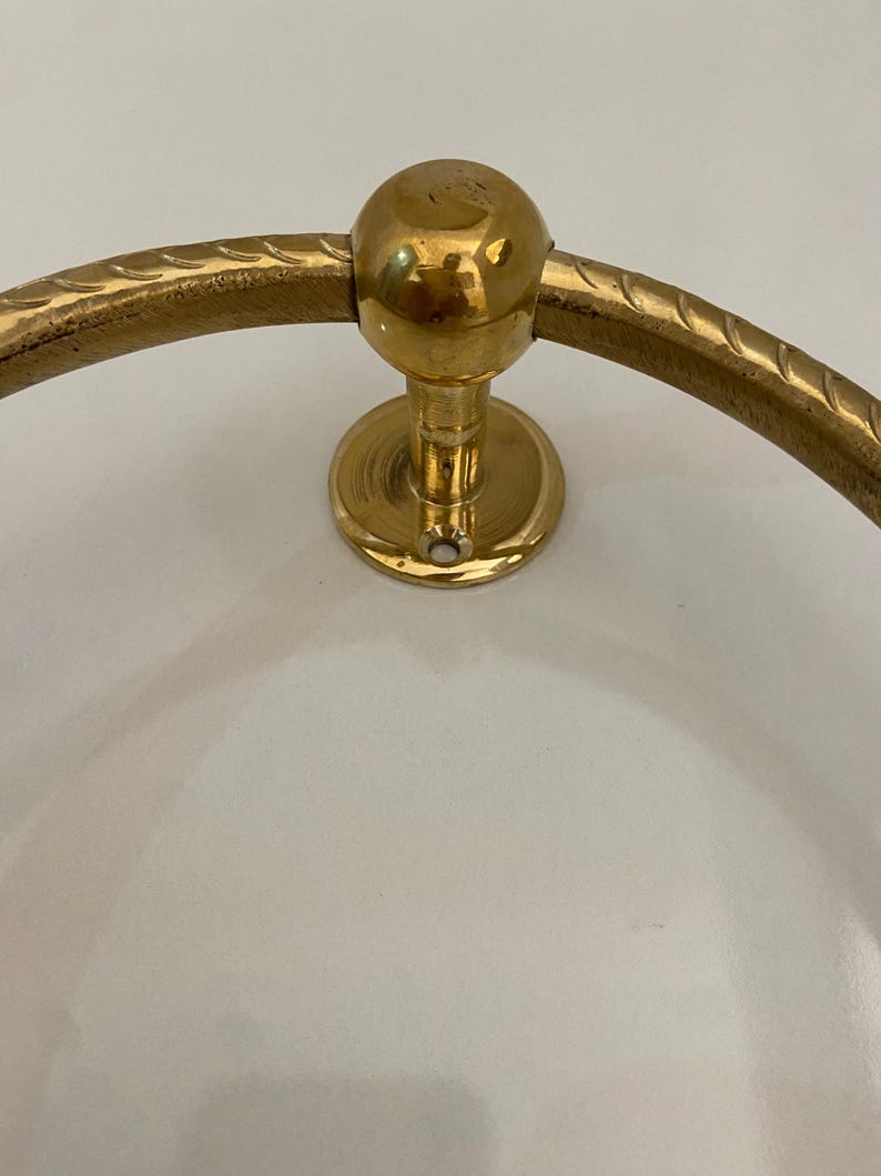 The ring is mounted on a circular base with a ball finial, The design is simple and elegant,The metal has a polished finish, giving it a shiny appearance, The ring is sturdy and well-made, suggesting durability and quality craftsmanship, This decorative piece would add a touch of classic style to any space