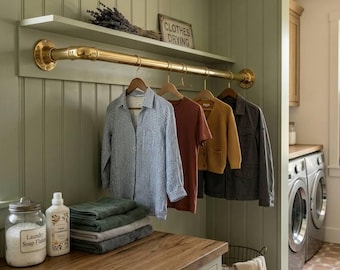 May include: A laundry room with a brass clothes rail and shelf. A blue and white checked shirt, a rust-coloured t-shirt, a yellow cardigan, and a grey jacket hang on wooden hangers. A sign reads "Clothes Drying".