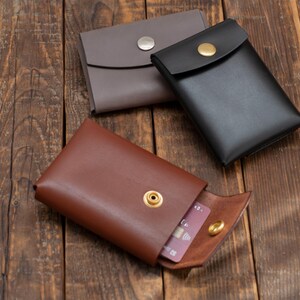 May include: Three leather wallets with a snap closure. The wallets are brown, gray, and black. One wallet is open and has a credit card inside.