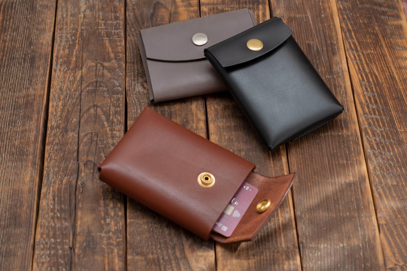 May include: Three leather wallets with a snap closure. The wallets are brown, gray, and black. One wallet is open and has a credit card inside.