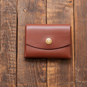 May include: A brown leather wallet with a brass button closure. The wallet is on a wooden surface.