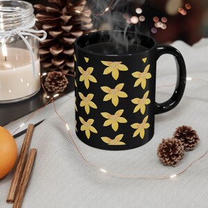Könnte beinhalten: Schwarze Kaffeetasse mit gelbem Blumenmuster. Die Tasse ist mit Kaffee gefüllt und Dampf steigt aus der Oberseite auf.