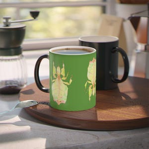 May include: A green coffee mug with a black handle features a watercolor illustration of two stick insects on a green background.